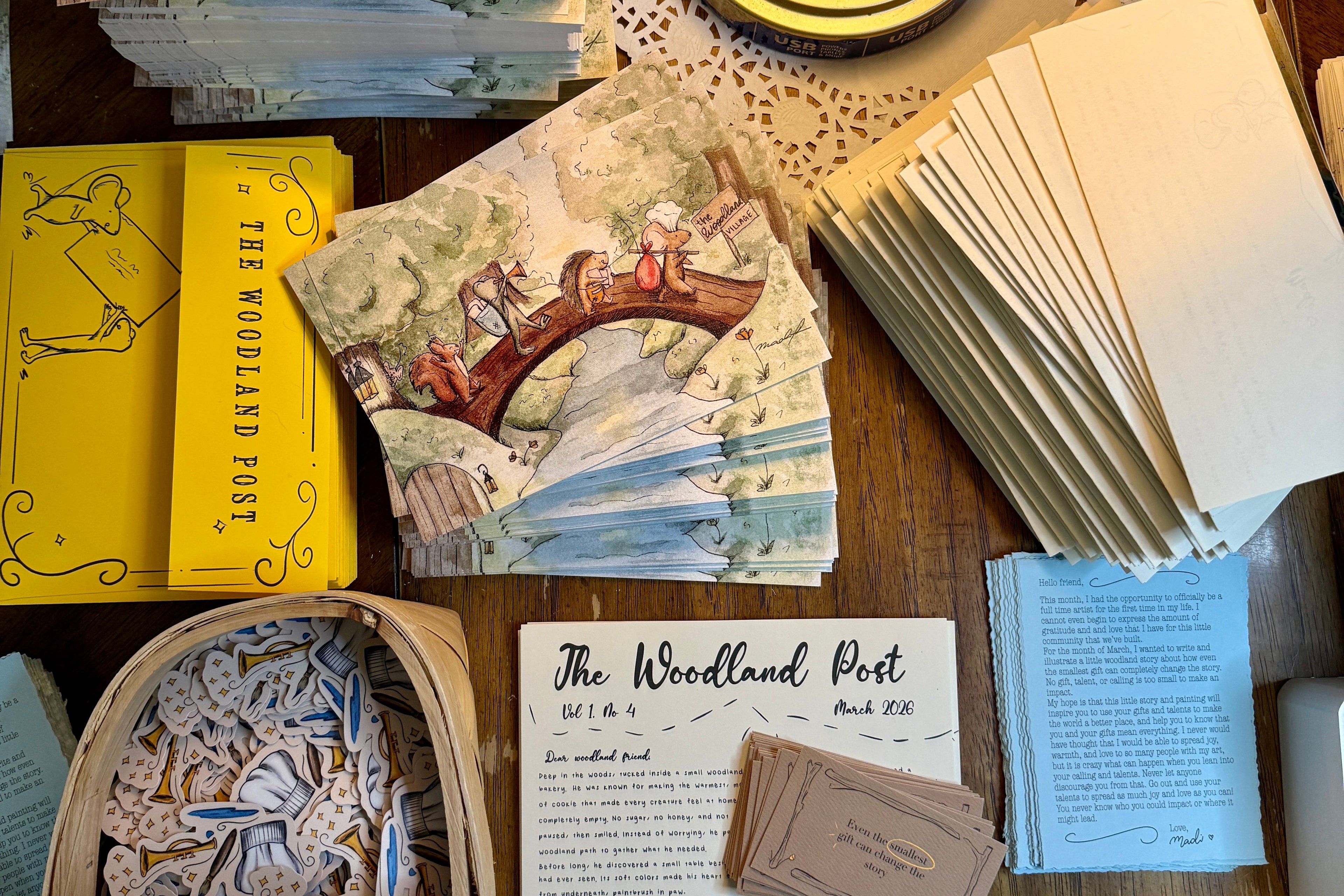 Collection of art, cards, and stationery items on a wooden surface with a lamp.